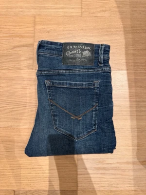 U.S Polo Assn Jeans - Snygga jeans från U.S. Polo Assn i klassisk blå denim med lätt slitna detaljer. Skön passform som sitter otroligt bra. Använda men fortfarande i väldigt gott skick (9/10). Kontakta angående storlek innan köp.  Säljs då de inte kommer till användning. Hör gärna av dig vid fler frågor eller funderingar!