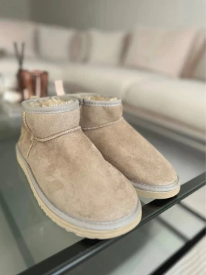 Beige UGGs - Säljer ett par klassiska beige UGGs. Skorna har låg skaftlängd och UGG-logga baktill. Aldrig använda då ja fick de i present 