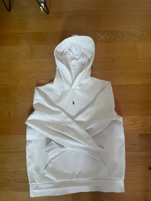 Vit hoodie från Polo Ralph Lauren - Vit hoodie från Polo Ralph Lauren med klassisk broderad logga på bröstet. Hoodien har känguruficka och ribbade muddar. Perfekt för en clean och stilren look. Materialet känns mjukt och bekvämt mot huden.