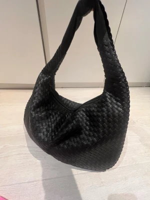Svart flätad väska - Snygg svart axelväska med flätad design och mjuk struktur Väskan har ett rymligt huvudfack med dragkedja och innerficka. Aldrig använd 