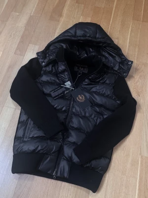 Marcél Classic Hybrid Jacket - Marcél Classic 02 i helsvart med quiltad pufferkropp och stickade ärmar. Avtagbar luva, lyxiga microfleecefickor och äkta läderdetaljer runt fickorna — premium finish som syns och känns. Perfekt för höst/vinter, kyliga vårdagar och svala sommarnätter — en jacka du bär hela säsongen. Finns i flera storlekar — skriv din längd och vikt så hjälper jag dig hitta den perfekta passformen! Säljer direkt för ett bättre pris än butik. Kan även köpas via www.nordens.store med Klarna & Paypal. 📦 Spårad frak