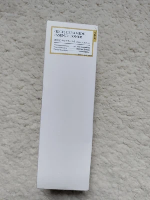 Rice Ceramide Essence Toner 250ml - Rice Ceramide Essence Toner från The Face Shop i en vit, rektangulär förpackning. Tonern innehåller risvatten och ceramider som återfuktar och stärker huden. Förpackningen är stilren och minimalistisk, perfekt för dig som gillar koreansk hudvård.