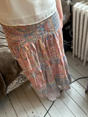 Långkjol med mönster - Säljer en flowy långkjol med mönster i rosa, blått och gult som även kan användas som en bandeau klänning. Kjolen har smock i midjan, så passar storlek S-L skulle jag säga. Nyskick, endast använd några få gånger! Nypris 599kr från Marta du Chatéau. Säljer då den är för kort enligt mina preferenser (jag är 177 med långa ben). 