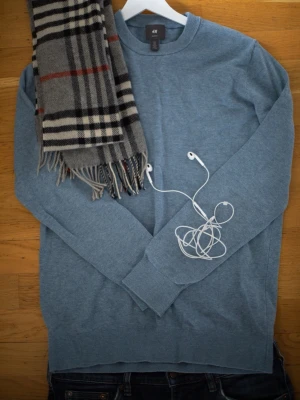 Blå stickad tröja från H&M - En stilren blå stickad tröja från H&M med rund halsringning och långa ärmar. Perfekt för lager-på-lager och enkel att matcha med jeans eller chinos. Tröjan har en klassisk passform och är mjuk mot huden.