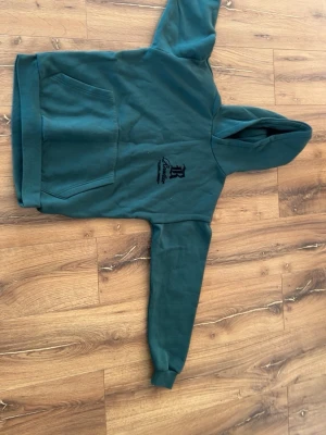 Grön hoodie från Black Squad - Mörkgrön hoodie från Black Squad i relaxed fit med stor magficka och huva. Tryck i svart på bröstet. Mjuk insida som känns skön mot huden. Perfekt för en chill och avslappnad stil. Pris kan diskuteras!