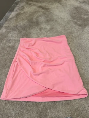 Rosa omlottkjol från Zara - Snygg rosa kortkjol från Zara med omlottdesign. Kjolen har en enkel och stilren look, perfekt för att skapa en trendig outfit. Tillverkad i ett mjukt material som känns bekvämt mot huden. Endast testad säljs pga fel storlek