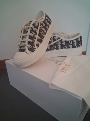 Dior Oblique låga sneakers - Snygga låga sneakers från Dior med klassiskt blått och vitt Dior Oblique-mönster. Skorna har vita snören, gummisula och detaljer med 'Christian Dior' på plösen. Perfekta för dig som gillar exklusiv och trendig streetstyle.