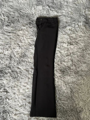 Svarta kostymbyxor med raka ben - Snygga svarta kostymbyxor med klassisk rak passform och pressveck. Byxorna har hällor för skärp och diskret stängning i midjan. Perfekta för en stilren look och passar till många olika outfits.