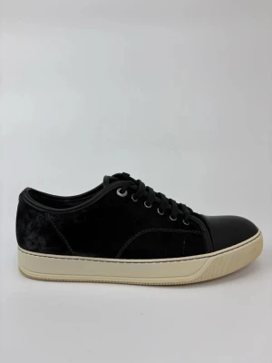 Svarta Lanvin sneakers med mockadetaljer - Stilrena svarta sneakers med ovandel i mocka och tåparti i slätt läder. Skorna har svarta skosnören, silverfärgade öljetter och en kontrasterande vit sula. Perfekta för en clean och modern look.
