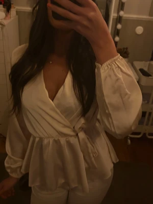 Champagnefärgad/ beige omlottblus med knytband från Missay i storlek S men passar även XS - Stilren champagnefärgad/beige omlottblus med knytband i midjan och v-ringad hals. Blusen har långa ärmar med resår vid ärmslut och ett lätt glansigt material som ger en elegant känsla. Perfekt att matcha med jeans eller kjol för en trendig look. Aldrig använd utan prislapp!