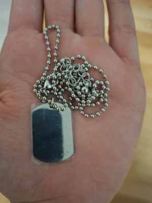 Silverfärgat dog tag-halsband Ur&Penn - Stilrent halsband från Ur&Penn med en silverfärgad dog tag-bricka och kulkedja. Halsbandet har en modern och minimalistisk design, perfekt för att ge din outfit en cool touch. Tillverkat i metall med pärlformad kedja.