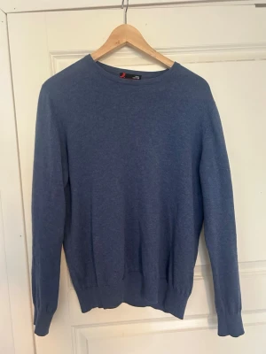 Blå basic tröja med rund hals - En stilren blå tröja med rund halsringning och långa ärmar. Tröjan har ribbade muddar vid ärmslut och nederkant, vilket ger en snygg passform. Perfekt att matcha med jeans eller chinos för en enkel och clean look.