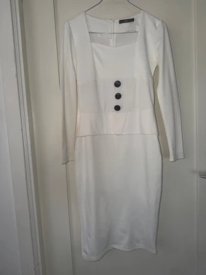 Vit långärmad klänning med knappar - Stilren vit klänning från Zara Basic med lång ärm och tre dekorativa svarta knappar framtill. Klänningen har en fyrkantig urringning och figurnära passform. Perfekt för dig som gillar minimalistisk design och vill sticka ut med enkla detaljer.