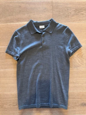Grå pikétröja från John Henric - Snygg grå pikétröja från John Henric med klassisk krage och tre knappar framtill. Tillverkad i mjukt material som känns skönt mot huden. Perfekt till jeans eller shorts för en clean och enkel look.