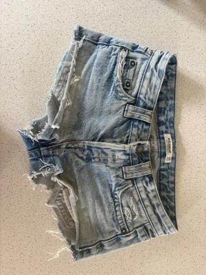 Lågmidjade jeansshorts från Pull&Bear - Säljer pga att dom inte passar mig!💓 Säljer ett par ljusblå jeansshorts från Pull&Bear med råa, fransiga kanter och slitningar. Shortsen har klassisk femficksdesign, bälteshällor och knappgylf. Perfekta för sommardagar och en avslappnad stil.