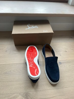 Marinblå mocka loafers  - Snygga marinblå loafers i mocka med vit sula och ikonisk röd undersida. Skorna har CL-logga broderad på ovansidan och en stilren, modern design. Perfekta för dig som vill sticka ut med exklusiva detaljer och lyxig känsla.                                Pris kan diskuteras!