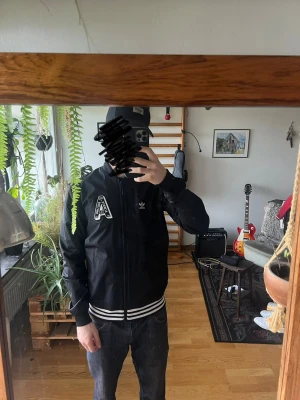 Tunn svart Adidas bomberjacka med patch - Svart bomberjacka från Adidas. Rätt tunn och inte så varm, bra till sommarkvällar. Möts upp i Stockholm 