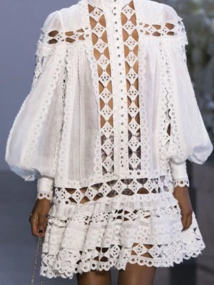 Vit spetsklänning med volang - Superfin vit kort klänning med volanger och detaljerad spets. Klänningen har långärmade puffärmar, hög hals och genombrutna partier som ger en unik look. Perfekt för dig som vill sticka ut med en romantisk och trendig stil.