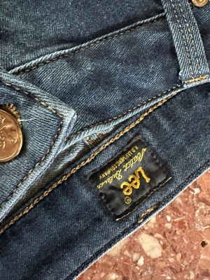 Mörkblå Lee jeans med smal passform - Säljer ett par mörkblå jeans från Lee med klassisk femficksdesign. Modell Marion straight W30 L35. Litet hål bak ena byxbenet, se bild. 