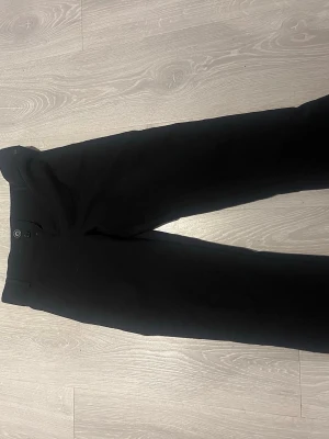 Svarta kostymbyxor med raka ben - Stilrena svarta kostymbyxor med raka ben och klassisk passform. Byxorna har knäppning fram och fickor bak med knappdetaljer. Med fickor där bak