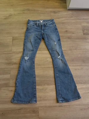 Blå bootcut jeans med slitningar Gina 14+ - Snygga blå bootcut jeans med slitna detaljer på framsidan och broderade bakfickor. Jeansen har klassisk femficksdesign och låg midja. Perfekta för dig som gillar en retro och avslappnad stil Inga defekter alls förutom att de kanske måste strykas!💓🌸