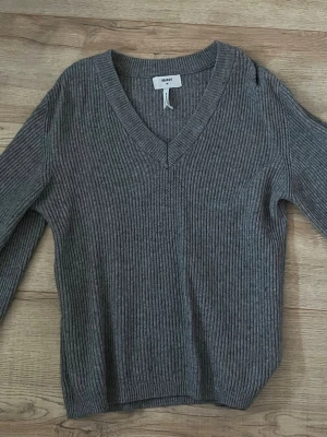 Grå ribbstickad tröja från Object - Säljer en grå ribbstickad tröja från Object med V-ringning och långa ärmar. Tröjan har en klassisk, enkel design och är perfekt för lager på lager. Materialet känns mjukt och följsamt, vilket gör den skön att bära hela dagen.