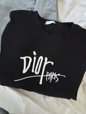 Svart sweatshirt från  - Snygg svart sweatshirt  med vit logga framtill i grafisk stil. Tröjan har rund halsringning och långa ärmar. Perfekt för dig som gillar streetwear och vill ha en stilren men ändå statement look.