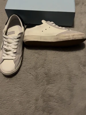 Vita Philippe Model sneakers - Snygga vita sneakers från Philippe Model med detaljer i ljusgrå mocka och klassisk låg siluett. Skorna har vita skosnören, gummisula och diskret logga på plösen. Perfekta för en clean och stilren look. Helt oanvända då jag skadade foten precis efter jag köpt dem och hann aldrig använda dem. Har bara stått och samla damm så nu är det dags att sälja dem. OBS skorna är inte smutsiga utan har sådana detaljer!