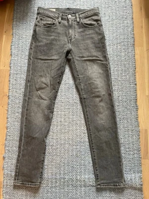 Grå Levis jeans - Säljer ett par grå jeans från Levis med klassisk femficksmodell och dragkedjegylf. Jeansen har en tvättad look och smal passform hela vägen ner. Perfekta för dig som gillar en stilren och enkel vibe.