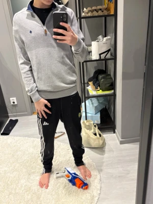 Grå halvzip-tröja från Morris - Snygg grå tröja från Morris med halv dragkedja och mörkblå krage. Tröjan har ett diskret Morris-emblem broderat på bröstet och ribbade muddar vid ärmslut och nederkant. Perfekt till jeans eller chinos för en clean look. Storlek L i barn fast det är xs