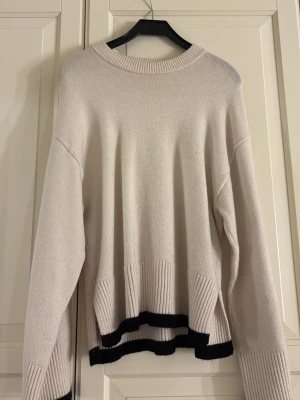 Beige stickad tröja Gina Tricot - Snygg beige stickad tröja från Gina Tricot med svarta ränder längst ner och vid ärmsluten. Tröjan har en avslappnad passform, rund halsringning och ribbstickade detaljer. Perfekt för lager-på-lager och enkel att matcha med jeans eller kjol.