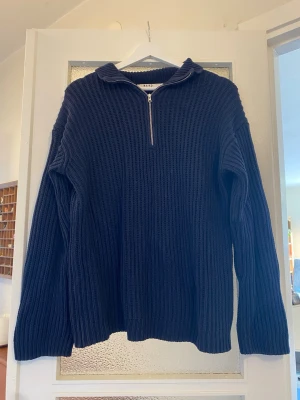 Mörkblå stickad tröja från NA-KD - Mörkblå stickad tröja från NA-KD med grov ribbstickning och halv dragkedja framtill. Tröjan har hög krage och långa ärmar, perfekt för lager på lager och en chill look. Materialet är mjukt och ger en avslappnad vibe.
