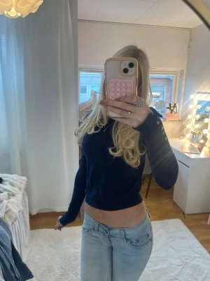 Mörkblå cropped stickad tröja - Snygg mörkblå stickad tröja i croppad modell med långa ärmar och dekorativa knappar vid ärmsluten. Perfekt till jeans för en avslappnad men trendig look. Tröjan har en enkel, stilren design och är mjuk i materialet.