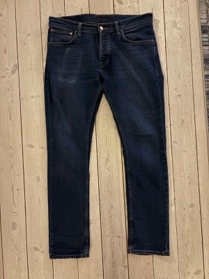 Mörkblå jeans från Nudie Jeans - Snygga mörkblå jeans från Nudie Jeans med klassisk femficksmodell och raka ben. Jeansen har subtila slitningar och kontrastsömmar. Tillverkade i mjuk denim som sitter skönt och passar perfekt till en avslappnad stil. Ägt dom i endast 1 månad. Nypris 1599kr.