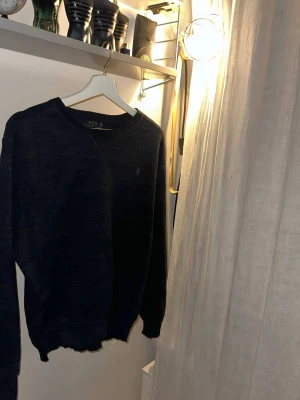 Mörkblå stickad tröja Polo Ralph Lauren - Snygg mörkblå stickad tröja från Polo Ralph Lauren med rund halsringning och diskret broderad logga på bröstet.  Riktigt bra skick med inga hål priset är inte hugget i sten  Nypris cirka  1200+                                                              STORLEK : MEDIUM HERR!