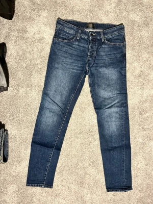 Blå slim fit jeans från Neuw - Snygga blå slim fit jeans från Neuw med klassisk femficksdesign och diskreta slitningar. Jeansen har normalhög midja, dragkedjegylf och är tillverkade i ett mjukt denimtyg med lite stretch för extra komfort. Perfekta till en avslappnad streetstyle-look.