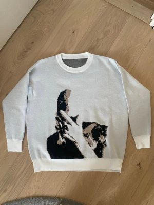 Vit stickad Frank Ocean tröja - Säljer en vit stickad oversized tröja med ett stort grafiskt motiv i svart, beige och brunt framtill. Tröjan har rund halsringning och ribbade muddar vid ärmslut och nederkant. Perfekt för dig som gillar Frank Ocean och  unika plagg med konstnärlig touch! Säljer då jag ej använder längre. Nypris: 900kr