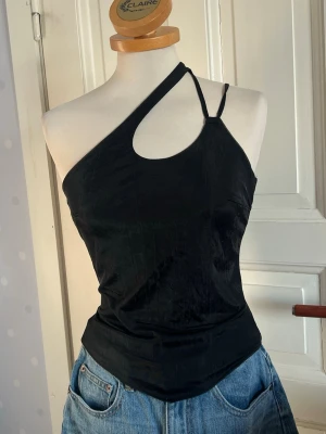 Svart oneshoulder top S - Trendig svart topp med asymmetrisk oneshoulder-design och dubbla smala axelband. Snygg och tight passform som framhäver figuren. Perfekt till jeans eller kjol för en cool look.