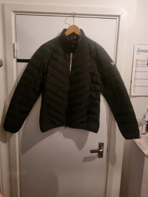 Svart pufferjacka från EA7 Emporio Armani -  ANVÄND MAX 10 GÅNGER. Snygg svart pufferjacka från EA7 Emporio Armani med diskret logga på bröstet och ärmen. Jackan har dragkedja framtill, hög krage och quiltat mönster. Perfekt för kalla vinterdagar och ger en stilren look.