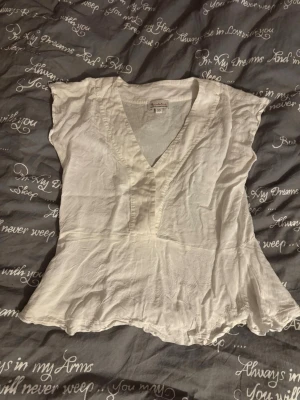 Vit blus med v-ringning från Bondelid - Säljer en luftig vit blus från Bondelid i storlek XS. Blusen har v-ringning, korta ärmar och lätt vågig nederkant. Tillverkad i ett tunt, mjukt tyg som känns skönt mot huden. Perfekt till jeans eller kjol för en avslappnad look.