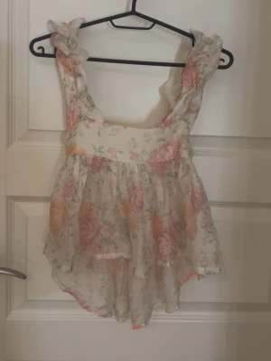 Blommig volangtop med rosett - Supersöt blommig linnetopp med volangdetaljer och breda axelband. Toppen har öppen rygg med stor rosett och är gjord i ett tunt, luftigt material. Perfekt för varma dagar! Använt 2-3 gånger💕💕