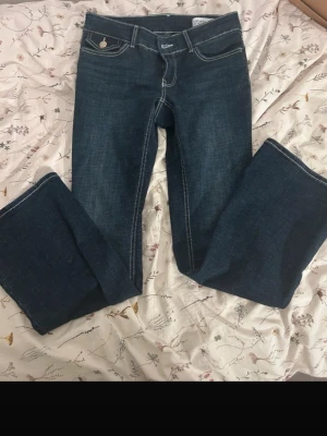 Mörkblå bootcut jeans med kontrastsömmar - Säljer ett par mörkblå bootcut jeans med vita kontrastsömmar och klassisk femficksdesign. Jeansen har normal midja och är tillverkade i ett mjukt denimtyg som sitter snyggt. Perfekta för en avslappnad men ändå trendig look.
