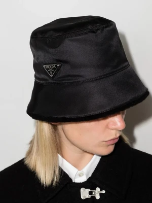 Svart bucket hat från Prada - Stilren svart bucket hat från Prada i glansigt nylonmaterial. Klassisk form med bred kant och ikoniska metalltriangeln med logotyp på sidan. Perfekt accessoar för en trendig och modern look. Pris kan diskuteras✅