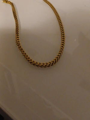 Guldpläterat kedjehalsband - Snyggt halsband i guldpläterad metall med fiskbensmönstrad kedja. Halsbandet har en klassisk och stilren design som passar perfekt till olika outfits. Perfekt accessoar för att lyfta din look.