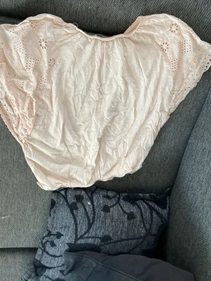 Ljusrosa offshoulder-blus från Mango - Söt ljusrosa offshoulder-blus från Mango med broderade detaljer och hålmönster på ärmarna. Tillverkad i ett lätt och luftigt material som känns skönt mot huden. Perfekt för en avslappnad och trendig look.storlek: 140 cm
