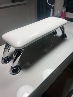 Vit handstöd för naglar - Snyggt och modernt handstöd för naglar i vit konstläder med kromade metallben. Perfekt för nagelbehandlingar och ger bra stöd för händerna under manikyr.