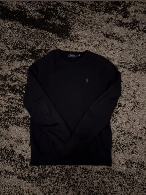 Mörkblå merino tröja Polo Ralph Lauren - Snygg mörkblå merino tröja från Polo Ralph Lauren med rund halsringning och diskret broderad logga på bröstet. Klassisk modell med långa ärmar. Perfekt för en stilren och enkel look.