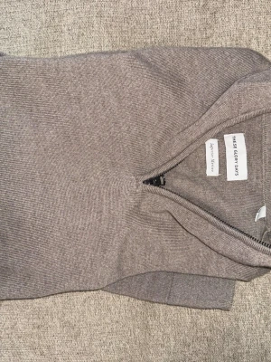 Beige stickad tröja med dragkedja - Stickad tröja i beige från These Glory Days med halv dragkedja framtill och ribbade detaljer vid krage och ärmslut. Tröjan har en enkel, stilren design och är tillverkad i ett mjukt, tunt material som passar perfekt för lager på lager.