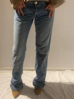 Blå raka jeans  - Säljer ett par klassiska blå jeans med rak passform. Jeansen har fem fickor och stängs med knapp och dragkedja. Tillverkade i ett slitstarkt denimtyg som ger en avslappnad look.