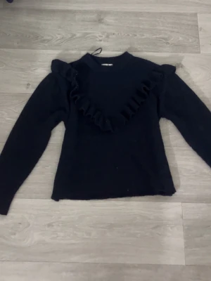 Marinblå stickad tröja med volang - Snygg marinblå stickad tröja från Gina Tricot med volangdetalj över bröstet och axlarna. Jag säljer tröjan pga att den inte kommit så mycket till användning!